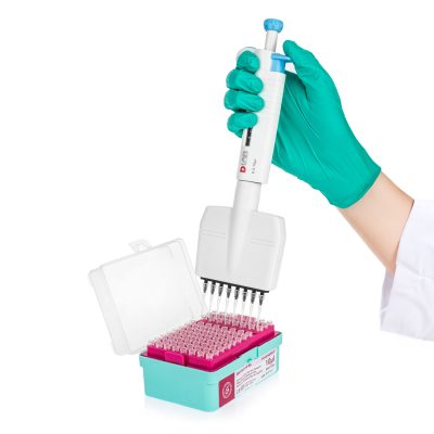 Ręka w zielonej rękawiczce trzyma pipetę nad stojakiem z probówkami.